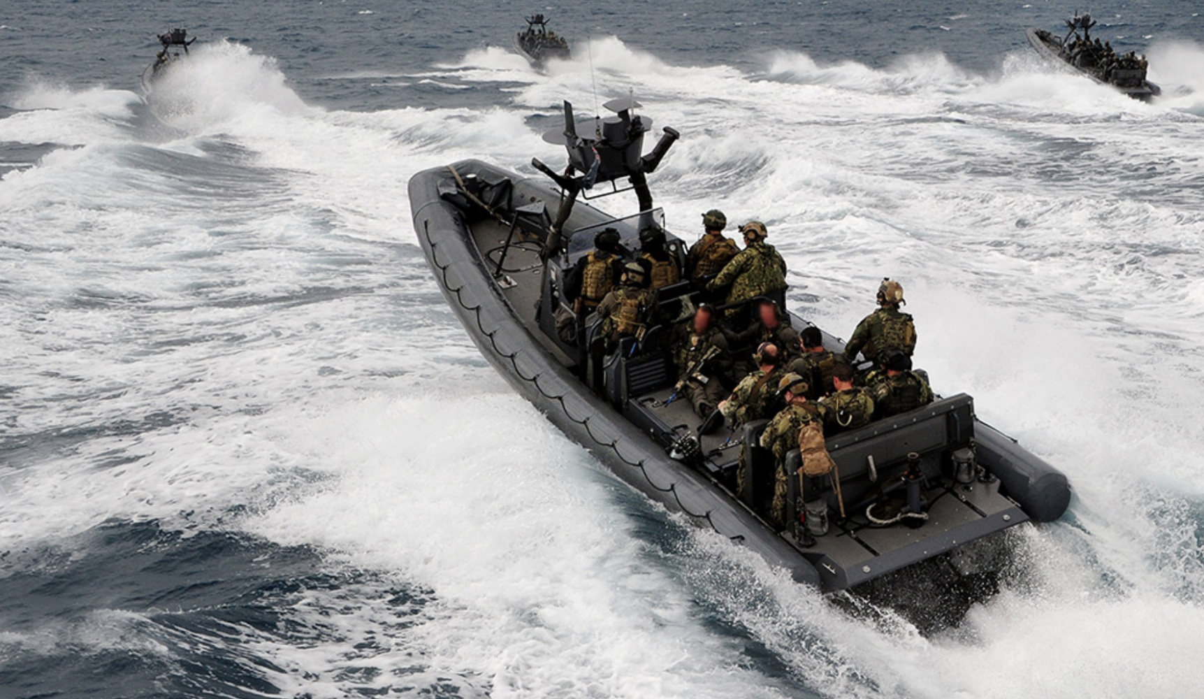 Military personnel on inflatable boats speeding over waves in open sea.