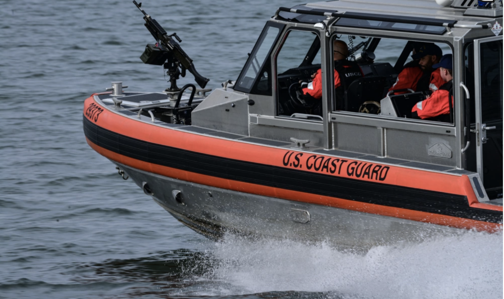 U.S. Coast Guard boat with crew and mounted gun on water.